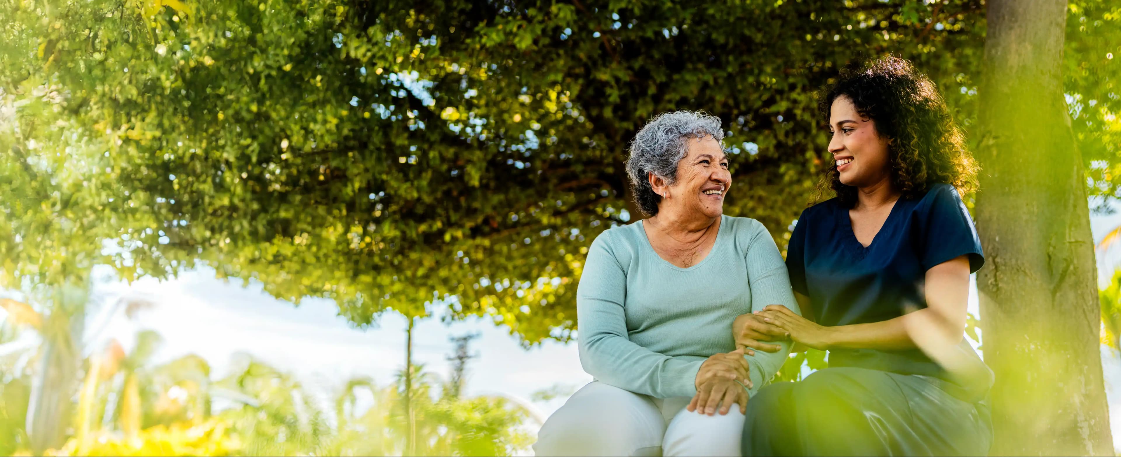 Mother and daughter sitting together in a park, smiling and sharing a moment of connection and care.