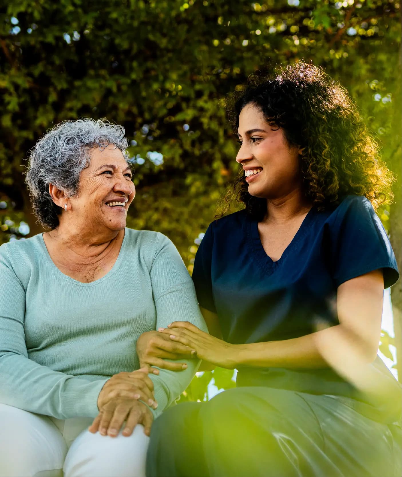 Mother and daughter sitting together in a park, smiling and sharing a moment of connection and care.