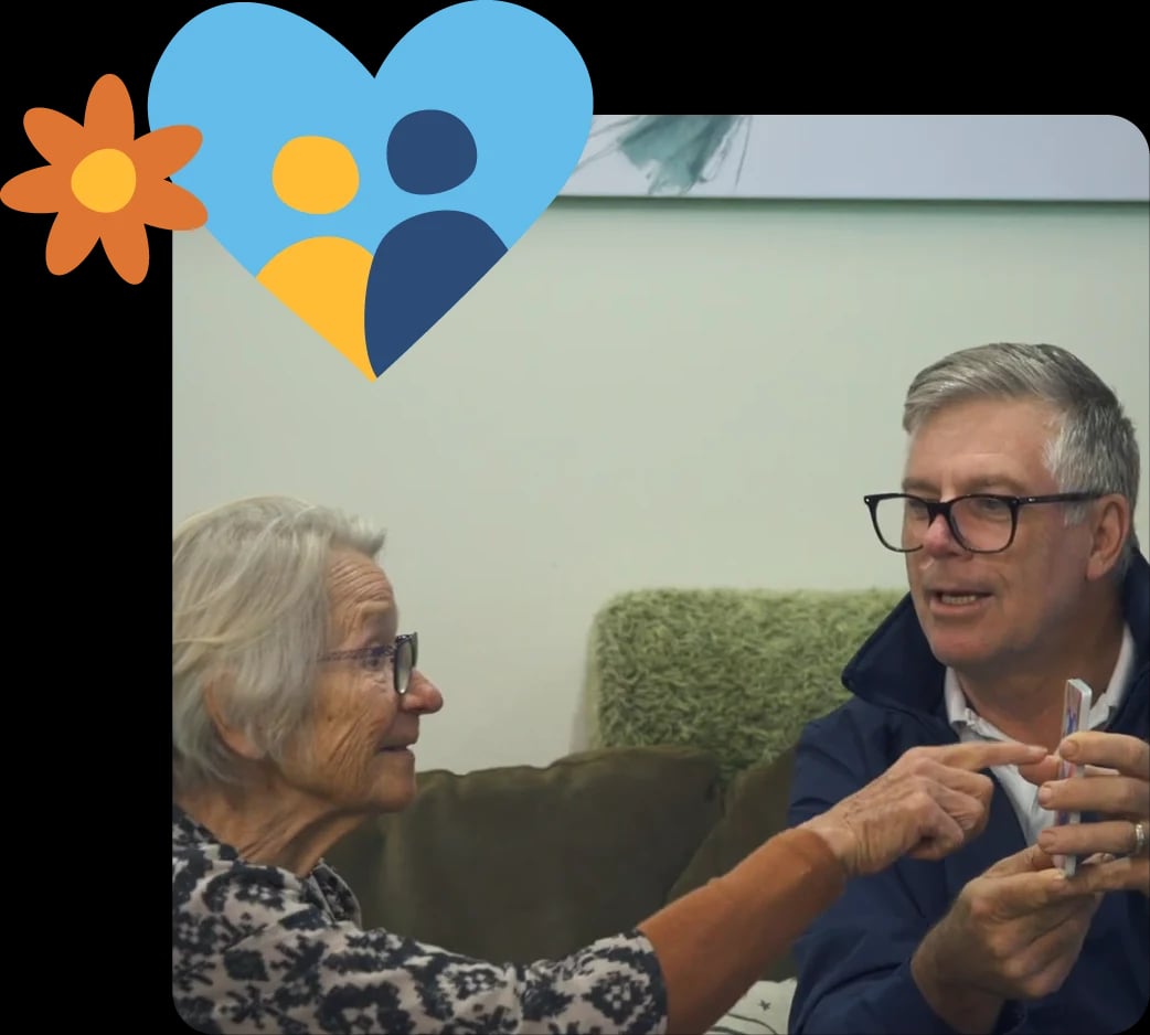 Older woman and man smiling and chatting on a couch in a home setting, representing supportive, client-led care