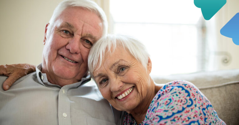 Smiling elderly couple sitting close together on a couch.